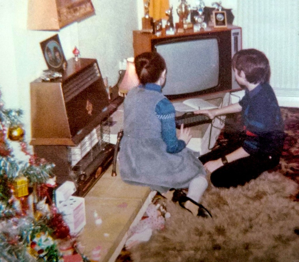 My sister and I sitting in front of the television on Christmas Day 1984, with a ZX Spectrum 48k in front of us. The edge of a Christmas tree, covered in baubles and decorations, in the foreground.