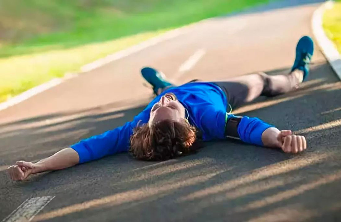 A male runner on his back, collapsed on the pavement.
