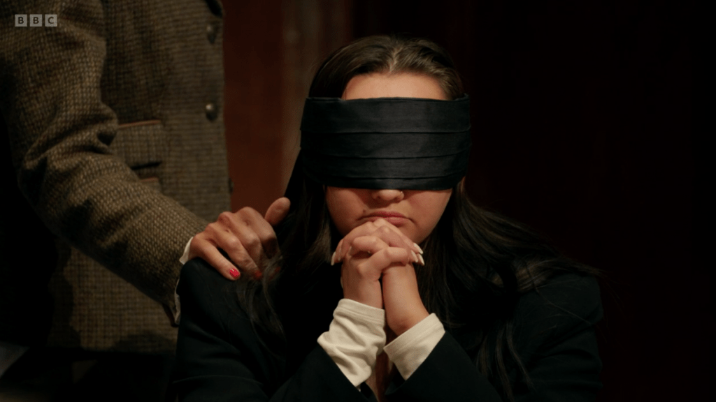 Blindfolded Traitors contestant Alyssa gets a squeeze on her shoulder from Claudia Winkleman to mark her as a traitor