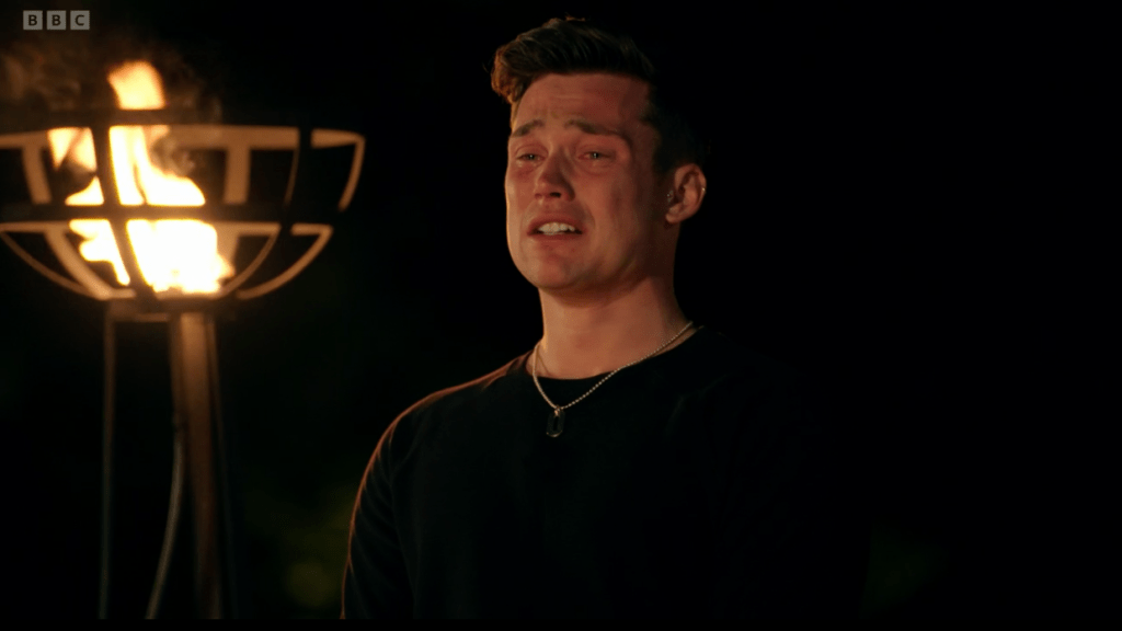 Aaron, a contestant on The Traitors, in tears during the final episode of the series with a flaming sconce in the background
